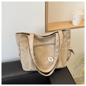 Detail of beige large capacity tote bag with good luck patch on a leather bench