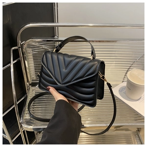 Close-up of black quilted shoulder bag with V-shaped stitching and golden hardware