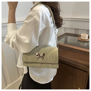 Detail of sage green quilted crossbody bag with silver butterfly charm and chain strap