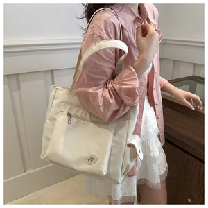 Detail view of a beige canvas tote bag featuring a front zipper pocket and side flap pocket