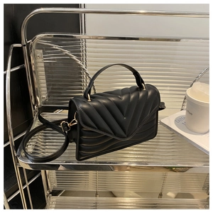 Detail of black V-quilted leather bag with gold hardware on a modern display shelf
