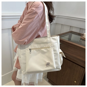 Detailed view of white canvas tote bag featuring a front zipper pocket and round lucky patch