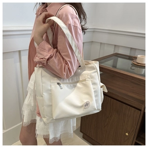Detail of beige nylon tote bag with front zipper pocket and side slots on a model