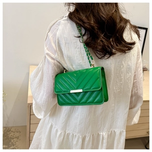 Detailansicht einer grünen Stepptasche mit goldener Schnalle auf einem weißen Kleid