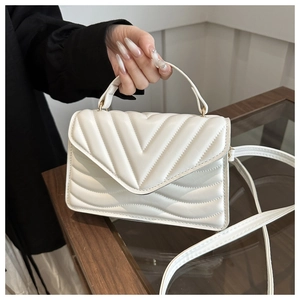 Detail of white quilted crossbody bag featuring V-shaped stitching and top handle strap
