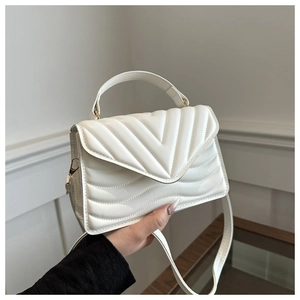 Detail of white quilted crossbody bag with V-shaped stitching and gold chain hardware