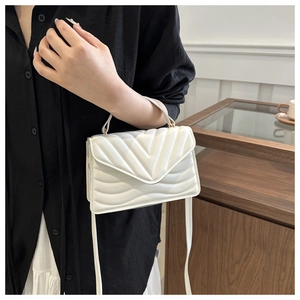 Detail of white quilted handbag with V-stitch pattern and top handle held by a model