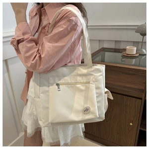 Detail of cream white canvas tote bag featuring a front zipper pocket and good luck patch