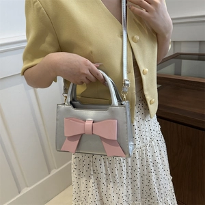 Silver metallic handbag with large pink bow featuring detachable shoulder strap