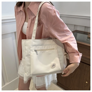 Detail of white nylon tote bag showing front zipper pocket and good luck round patch