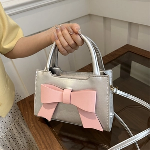 Silver glossy handbag with large pink bow featuring dual handles and a crossbody strap