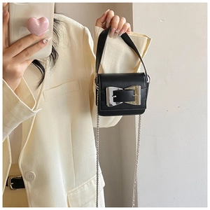 Detailed view of mini black crossbody bag featuring a large silver bow buckle and chain strap