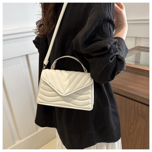 Detailed view of white quilted faux leather handbag with gold metal clasp and chain strap