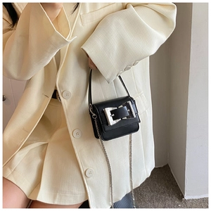 Detail of a chic black mini bag with silver buckle and metal chain strap on white blazer