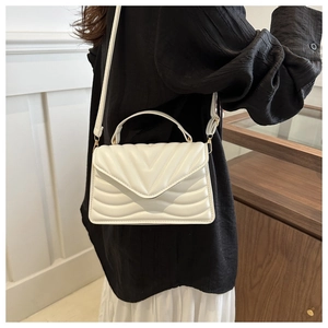 Close-up of white V-quilted small square crossbody bag with top handle and metal clasp