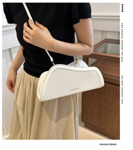 Detail of a white asymmetrical crossbody bag with golden logo lettering on a model