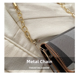 Close-up of golden metal lobster clasp and chain on a classic plaid canvas handbag