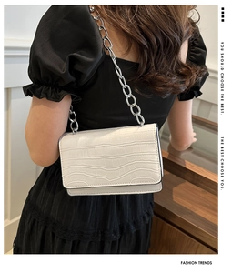 Detail view of white crocodile pattern crossbody bag with silver chain strap on model