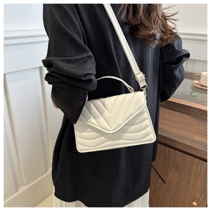 Detail of white quilted crossbody bag with adjustable strap worn by model on black outfit
