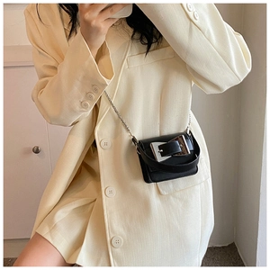 Detailed view of mini black crossbody bag with silver buckle on a yellow blazer