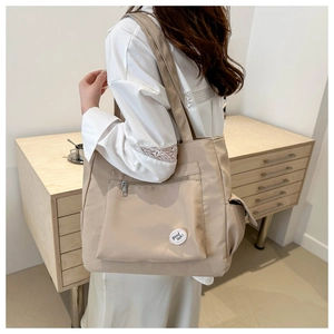 Detail of beige tote bag with front zipper pocket, side pouch and good luck label