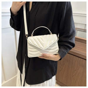 Detail view of a white quilted crossbody bag with golden hardware and top handle strap