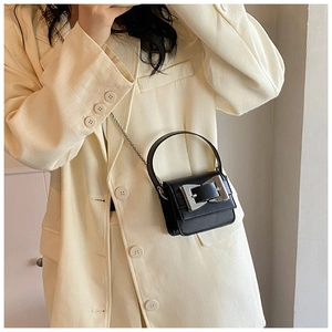 Detail of a black mini handbag featuring a bold silver square buckle and chain strap