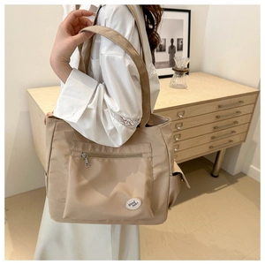 Close-up of beige nylon tote bag featuring front zipper pocket and good luck embroidery