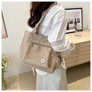 Detailed close-up of beige nylon tote bag with zip pocket and good luck embroidery