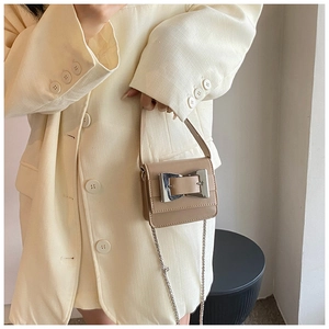 Mini beige crossbody bag with silver buckle and chain strap shown on a white blazer outfit