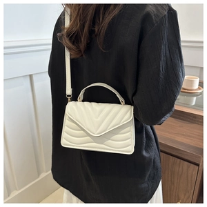 Close-up of cream quilted flap crossbody bag with V-pattern and chain handle on model