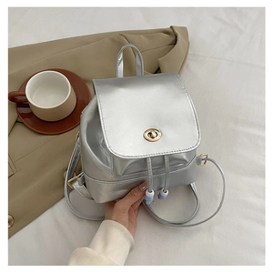 Close-up of a mini silver metallic backpack with a gold twist lock on a neutral blazer