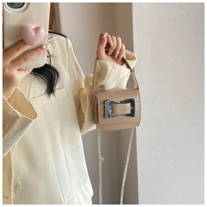 Detail of a khaki mini square bag with large silver buckle held by a model in a beige suit