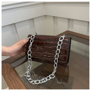 Detail of dark brown faux crocodile skin crossbody bag with glossy finish and silver chain
