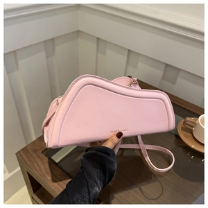 Unique pink irregular leather handbag with gold logo and shoulder strap on a table