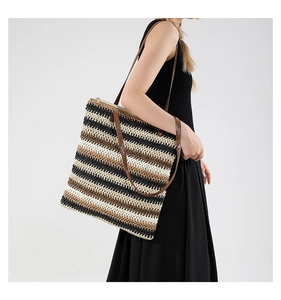 Detailed close-up of large woven straw tote bag with brown leather handles worn by a model