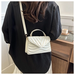 Model wearing a cream quilted crossbody bag with gold chain strap in a cozy home setting