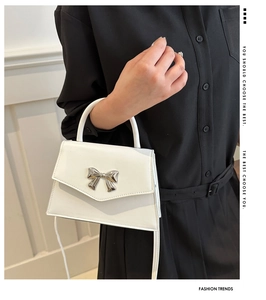 Detail of white mini handbag with silver metal bow and flap closure on black dress
