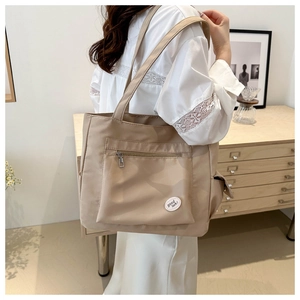 Detail of beige nylon tote bag featuring a zipped outer pocket and Good Luck patch