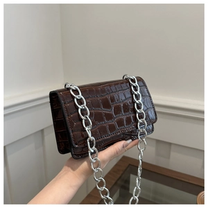Close-up of dark brown crocodile texture crossbody bag with silver chain strap details