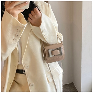 Close-up of mini khaki crossbody bag with a large silver bow buckle on beige suit