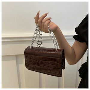 Detail of dark brown crocodile pattern leather handbag with thick silver metal chain strap