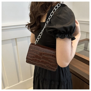 Detail of dark brown crocodile embossed texture and silver chain strap on crossbody bag
