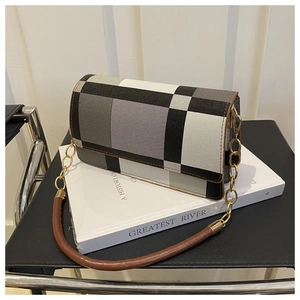 Close-up of a tricolor plaid flap shoulder bag with gold chain strap on a white book