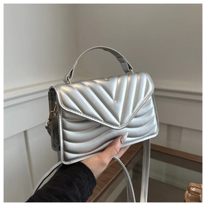 Detail of silver quilted crossbody bag with metallic V-stitch pattern and top handle