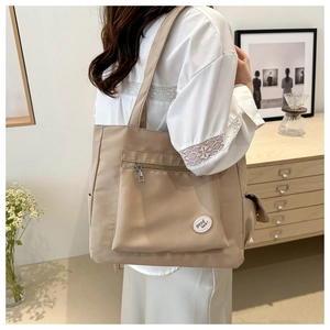 Side view of beige nylon tote bag featuring a front zipper pocket and side drawstring pocket