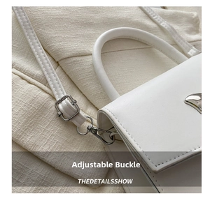 Detail of silver metal buckle and adjustable shoulder strap on white faux leather handbag