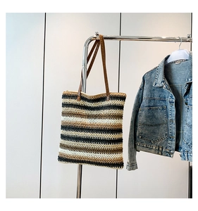 Detail of colorful striped woven tote bag with brown leather shoulder strap on a hanger