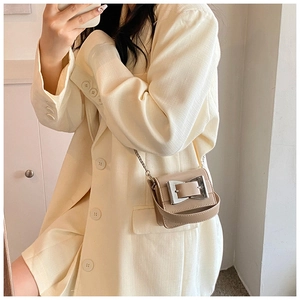 Detail of a beige mini crossbody bag with a large silver buckle and chain strap on a model