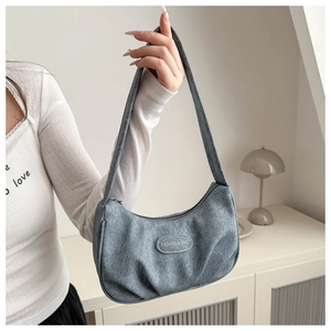 Detail of grey pleated shoulder bag with fashion text label and textured fabric surface